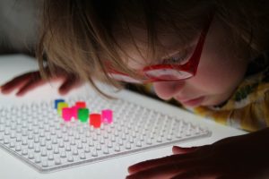 Frühförderung für Kinder mit cerebral bedingter Sehbeeinträchtigung – Kind betrachtet Perlen auf Steckbrett ganz nah