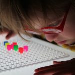 Frühförderung für Kinder mit cerebral bedingter Sehbeeinträchtigung – Kind betrachtet Perlen auf Steckbrett ganz nah
